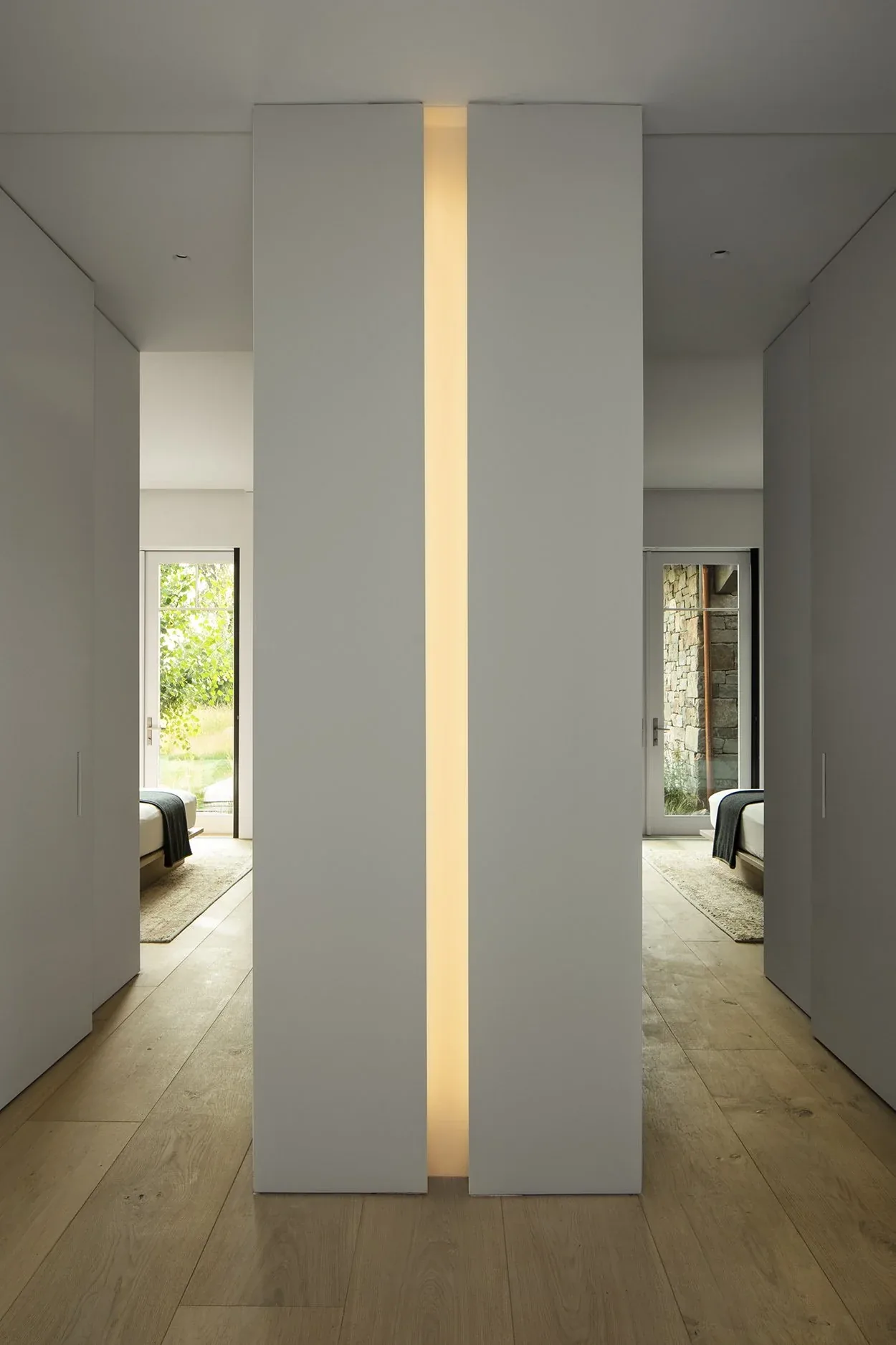 Hallway with wood plank floors and a vertical recessed light separating two white wall panels between bedrooms.