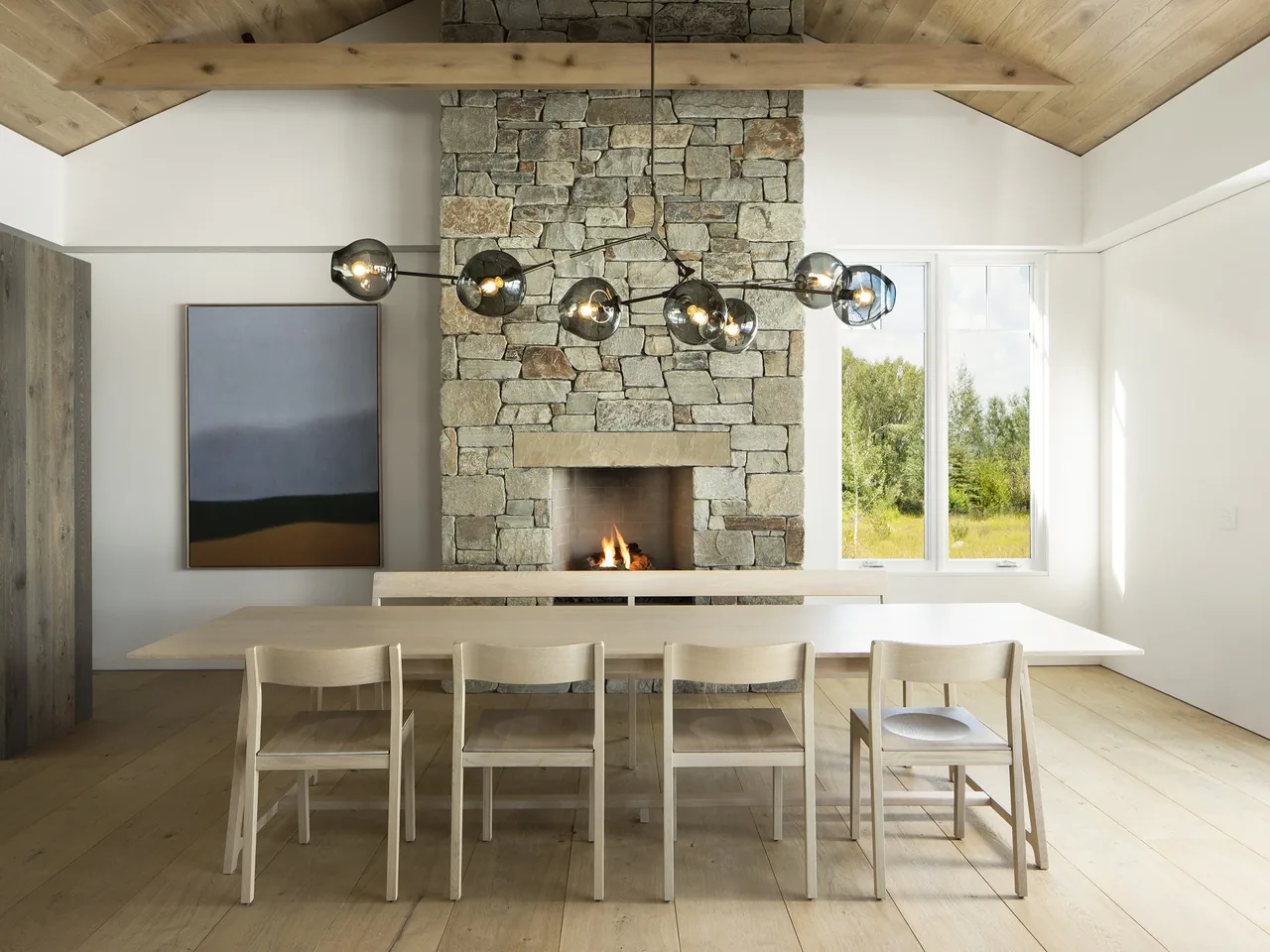 The dining area features a stone fireplace centered on a white wall with a wood plank vaulted ceiling and large window.