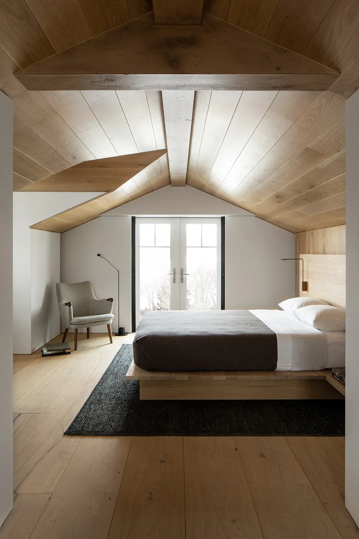 The bedroom features a wood plank ceiling with exposed beams, a floating bed, and French doors with black window frames.