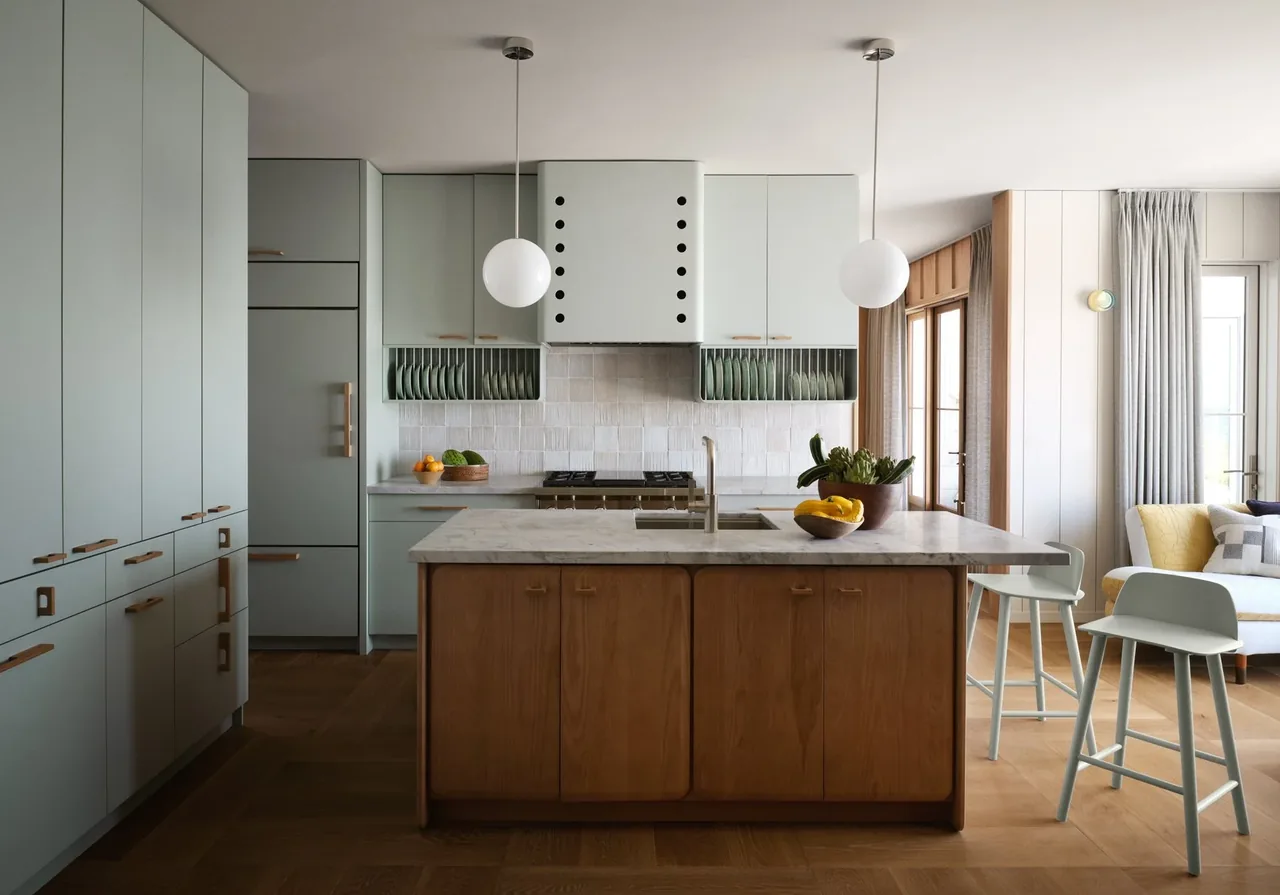 The kitchen features light blue cabinets, a wooden island with marble countertop, and two round white pendant lights.