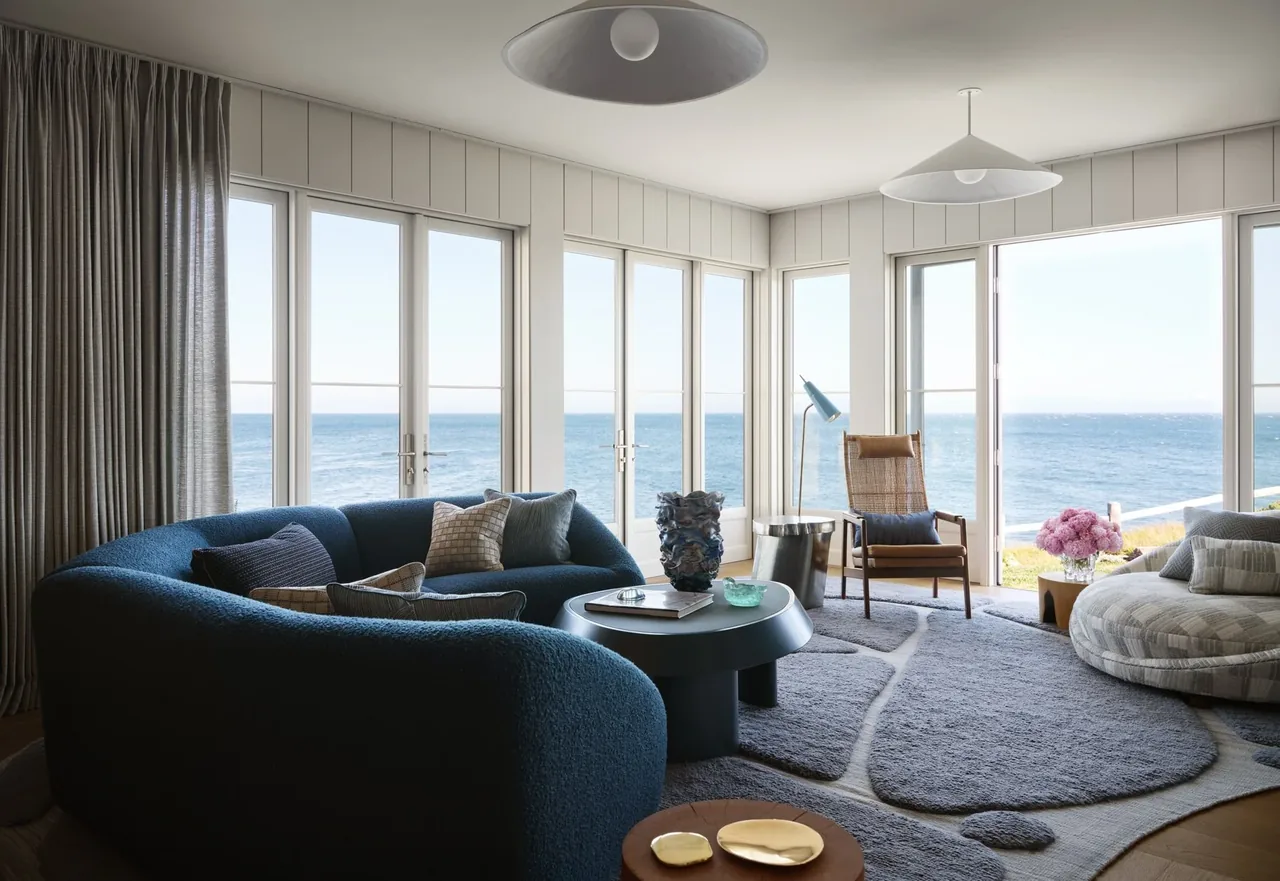 Living room with large glass doors offering an ocean view, featuring a curved blue sofa and modern furniture.