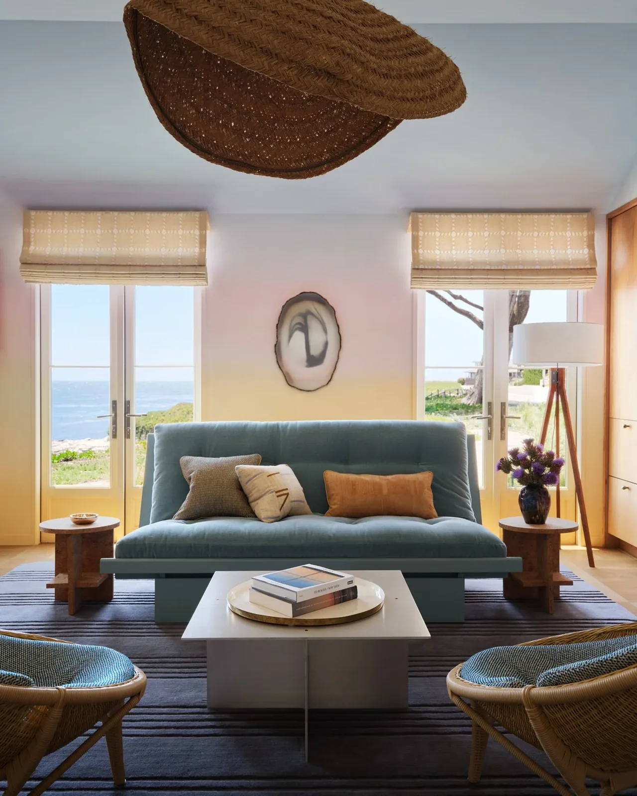Pacific Promontory living room by McGriff Architects features coastal views through glass doors with roman shades and blue upholstery.