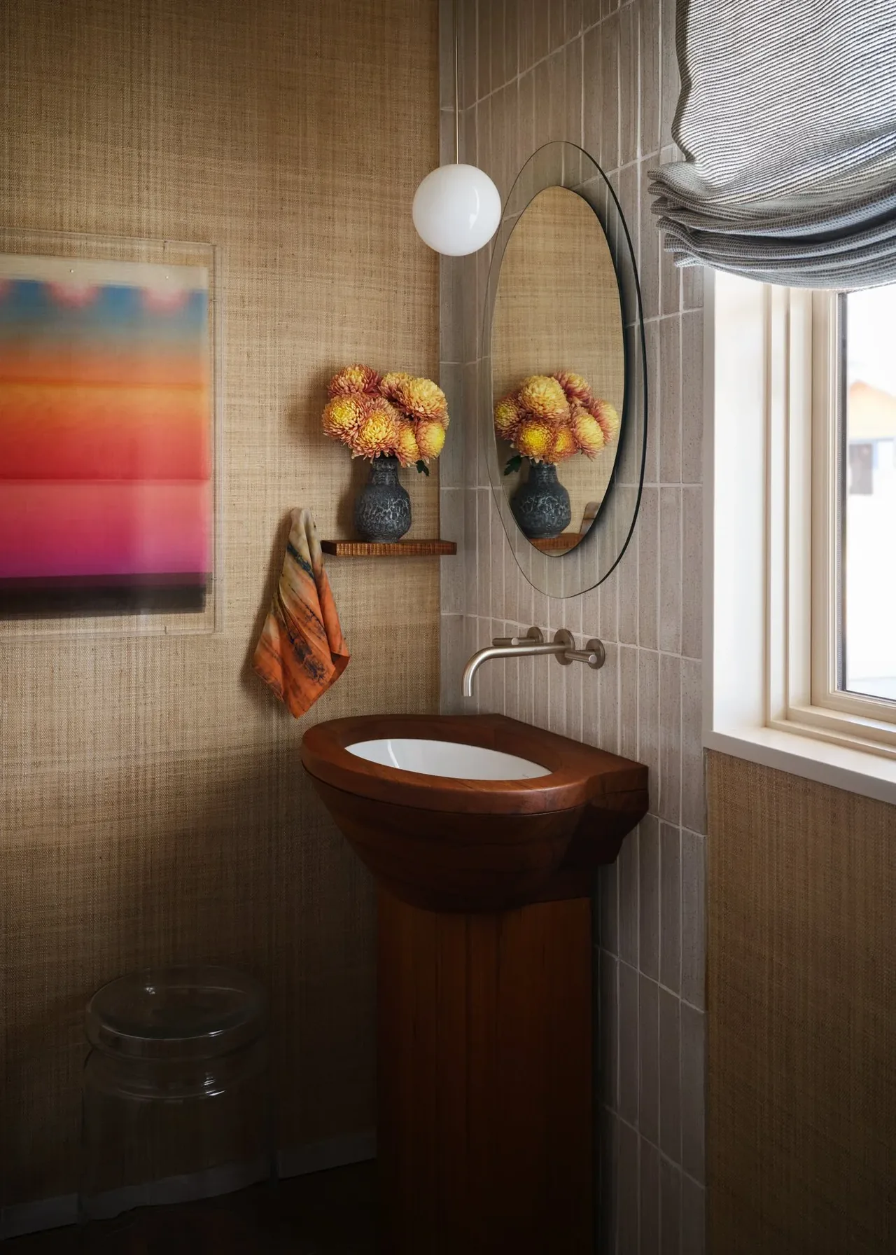 Bathroom with a wooden pedestal sink, round mirror, gray roman shade, and a hanging globe sconce.