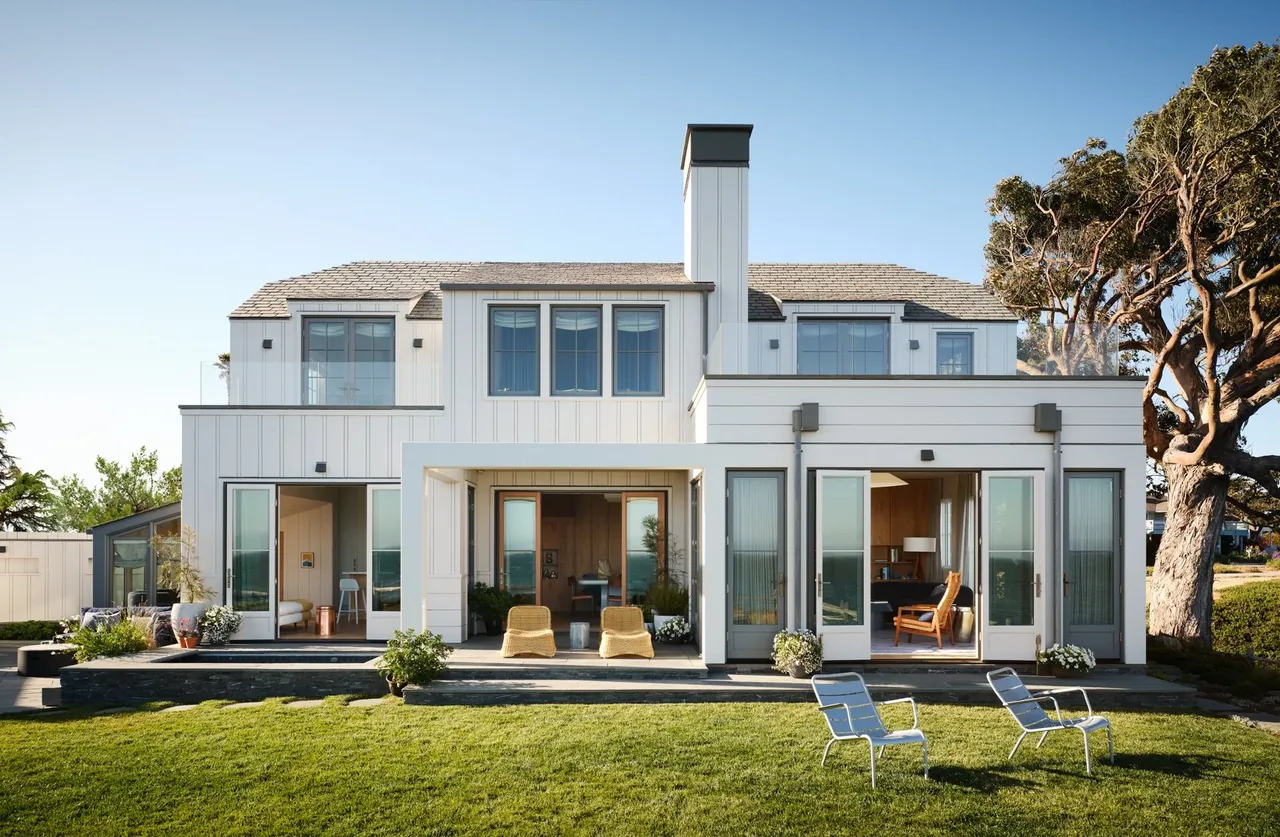 Rear exterior of the Pacific Promontory house featuring white wood siding, multiple glass doors, and a lawn with seating.