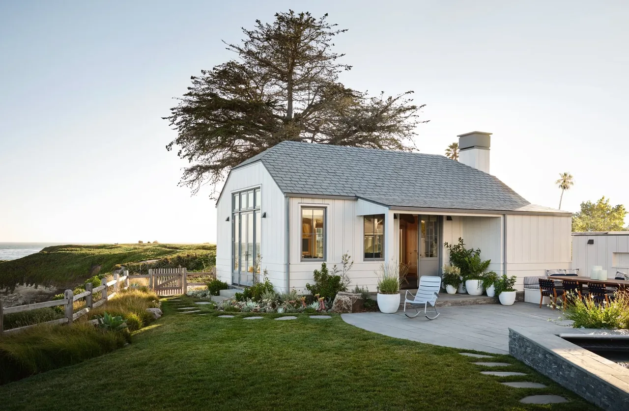 The Pacific Promontory project features a white house with a gambrel roof, vertical wood siding, and large windows facing a coastal landscape.