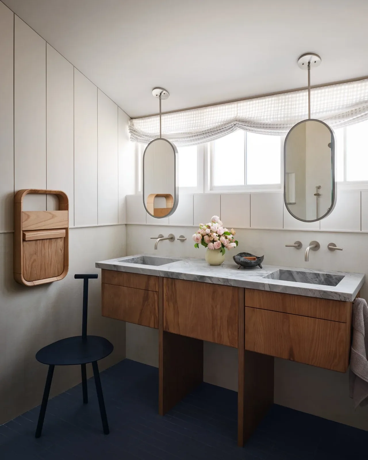 Bathroom features a double sink marble vanity with wooden cabinetry and oval pendant mirrors against soft natural light from windows.
