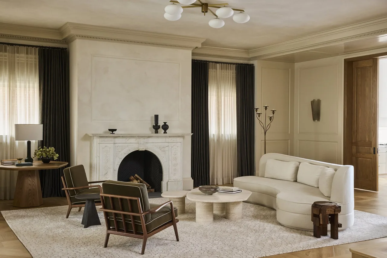Living room featuring a carved stone fireplace, curved sofa, and natural wood furniture with dark curtains.