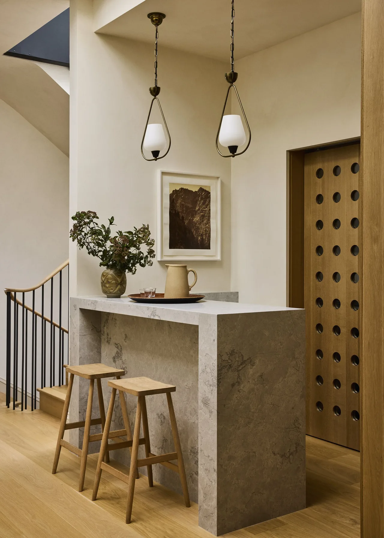 A modern kitchen island with light wood stools and brass pendant lights in a neutral-toned interior.