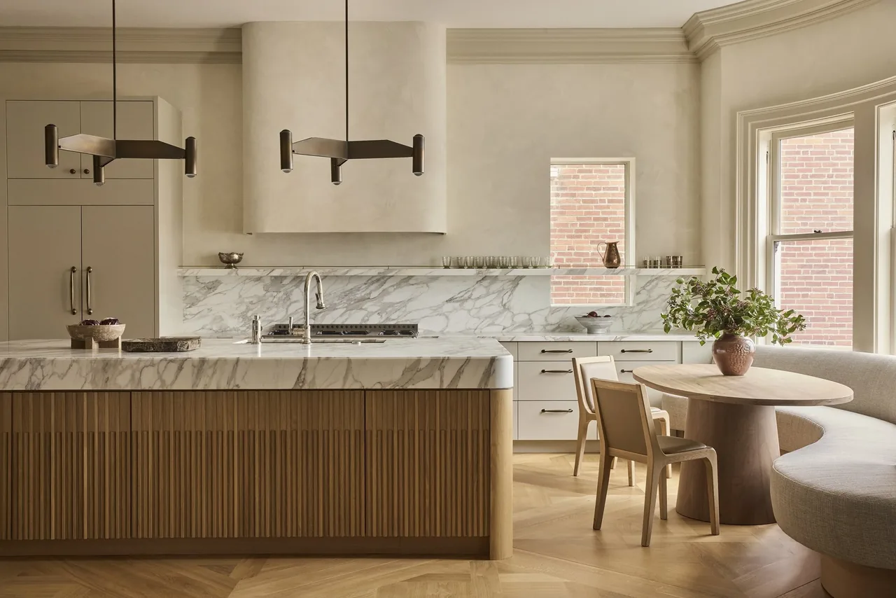 Modern kitchen featuring a large marble island with wood paneling and a built-in curved banquette seating area by the windows.