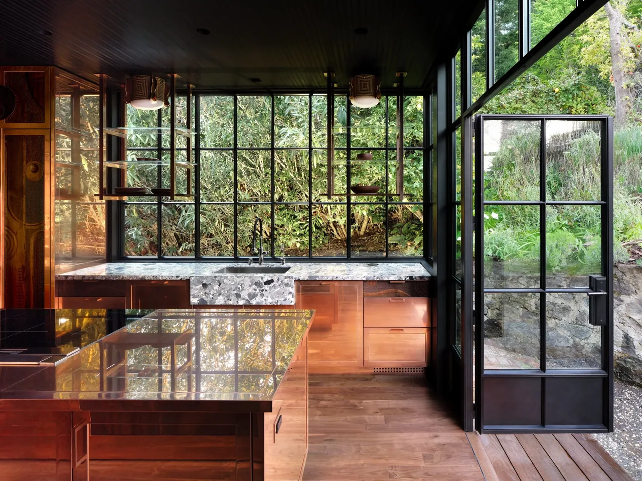 Kitchen in Gallery House with floor-to-ceiling black-framed windows and a door opening to outdoor greenery.