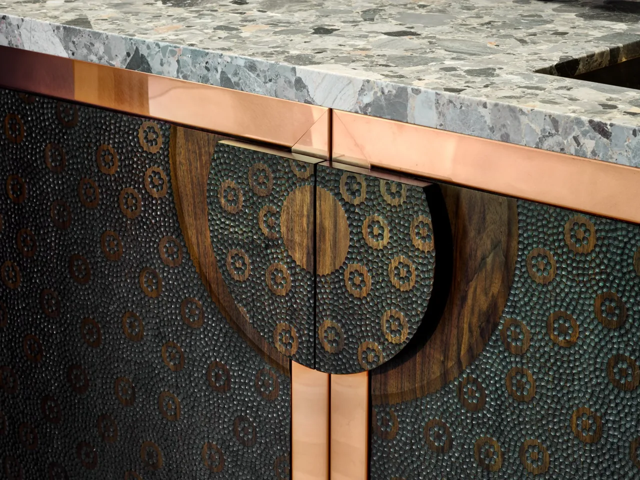 Textured copper cabinet doors with a patterned design under a stone countertop.