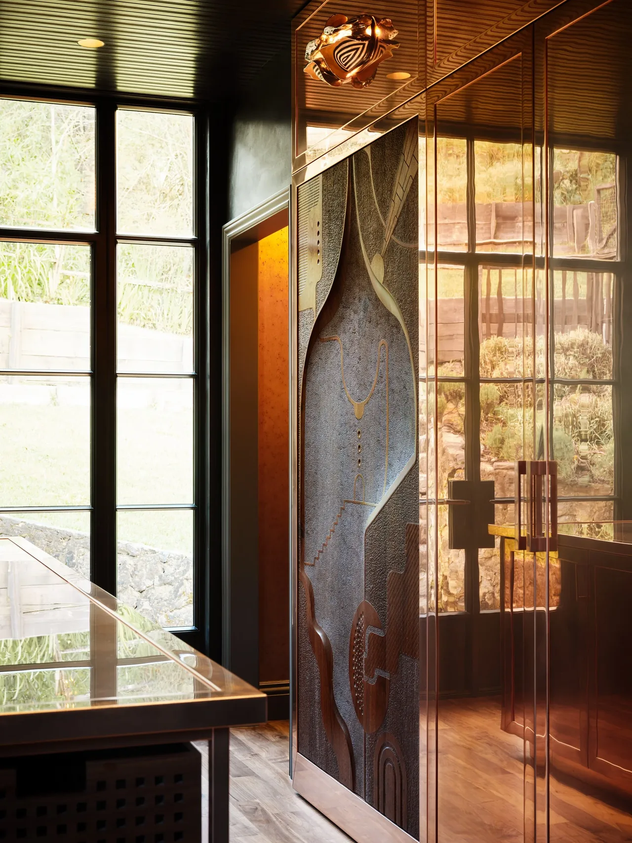 Copper cabinetry with textured panels in the kitchen reflecting outdoor views through grid-design windows.