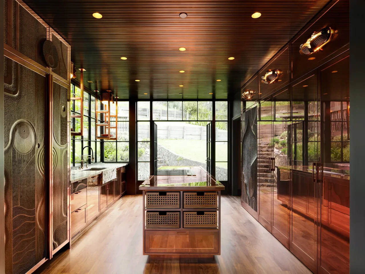 The Gallery House kitchen features copper cabinetry, a central island, and large windows with a view of landscaped steps outside.