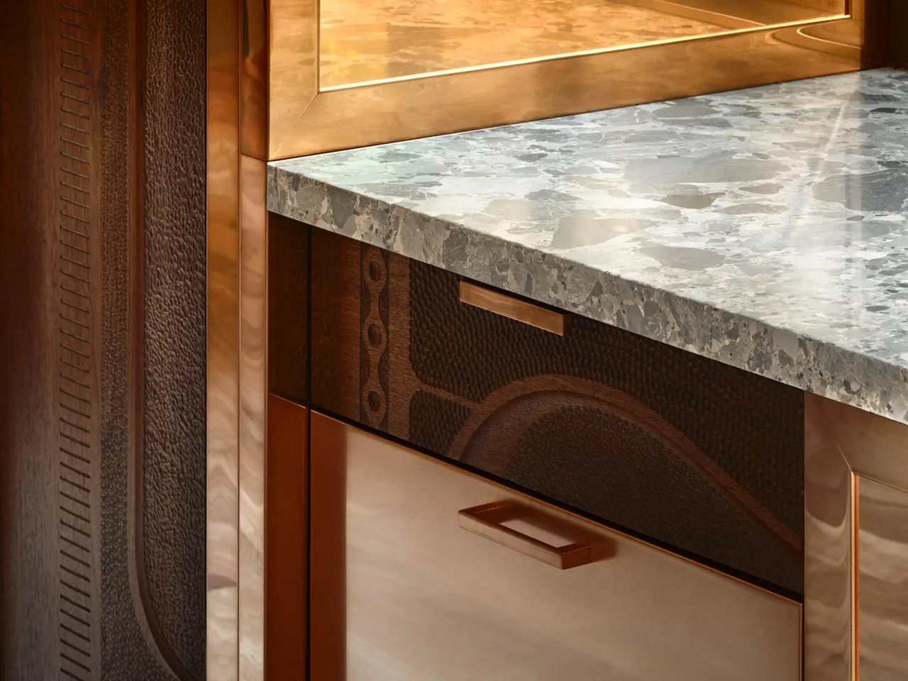 The kitchen features a patterned stone countertop paired with textured copper cabinetry panels.