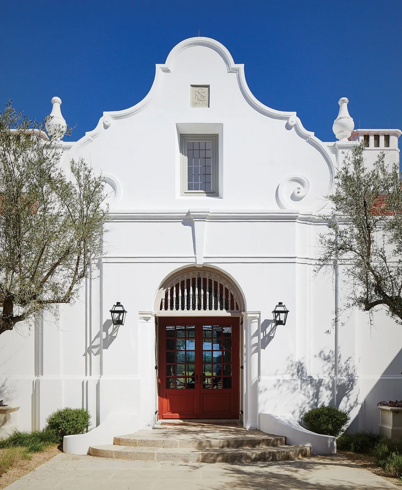 Facade of a residential building with white stucco walls and arched wooden double doors at Rancho Sabino Grande.