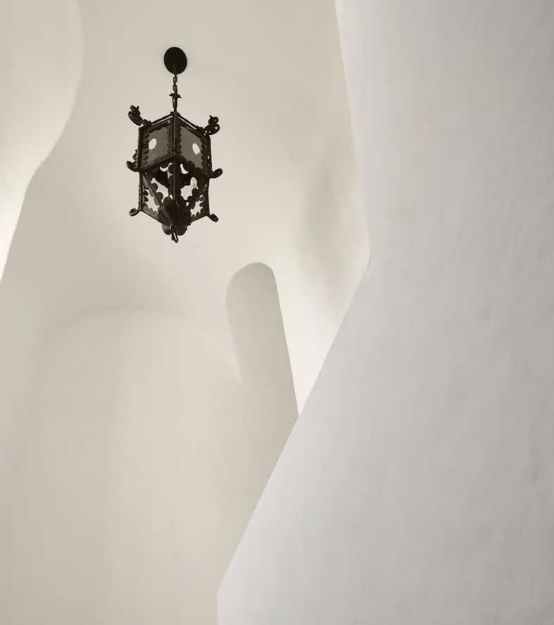 Ornate black pendant light hangs in a white plaster hallway with curved architectural details.