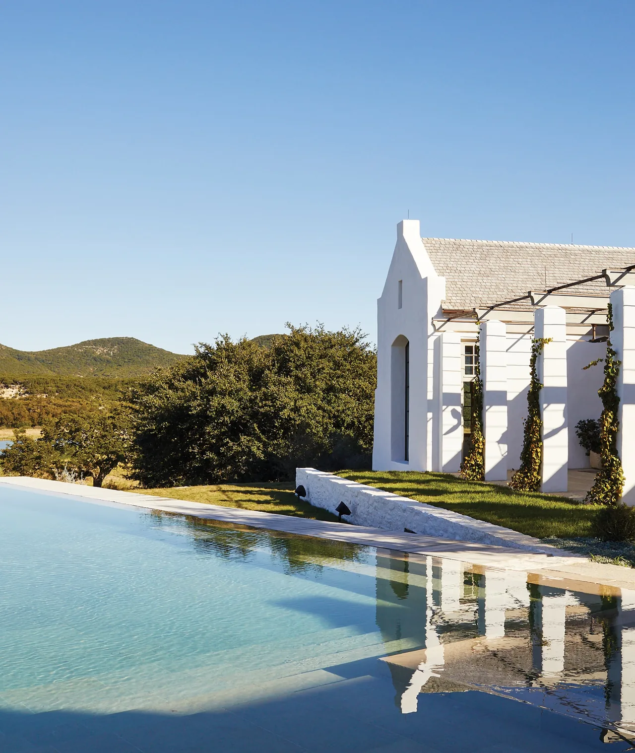 The Rancho Sabino Grande project features a white stucco exterior with a shingle roof and columned pergola beside an inviting pool.