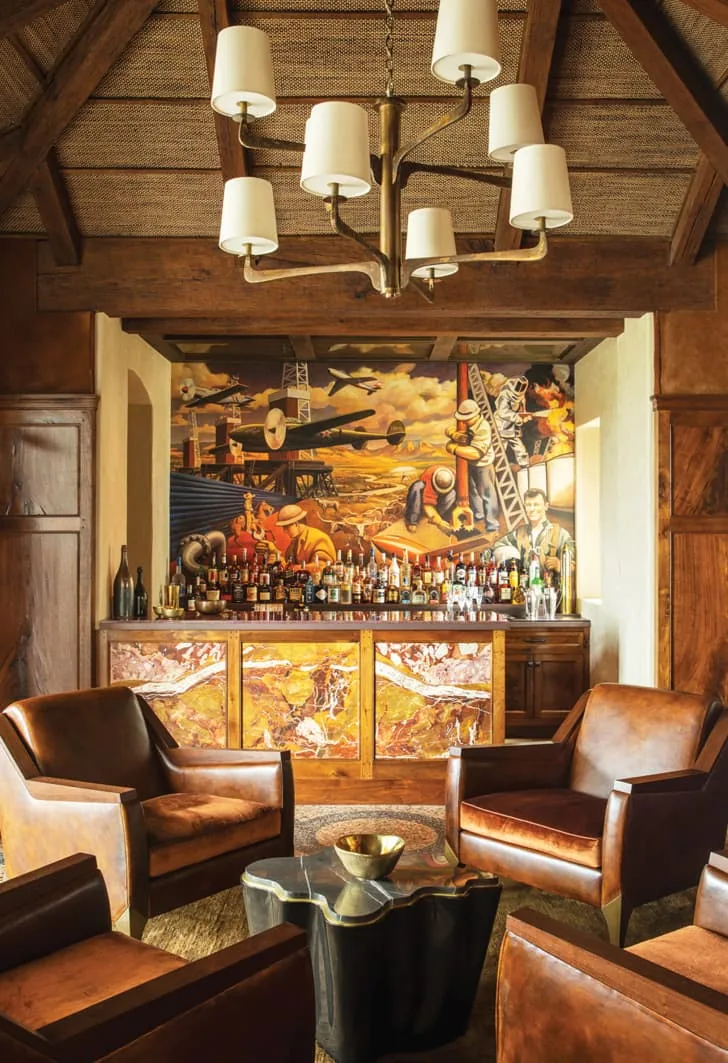 Lounge area in Rancho Sabino Grande features leather seating, a mural backdrop, and a decorative bar with amber stone panels.