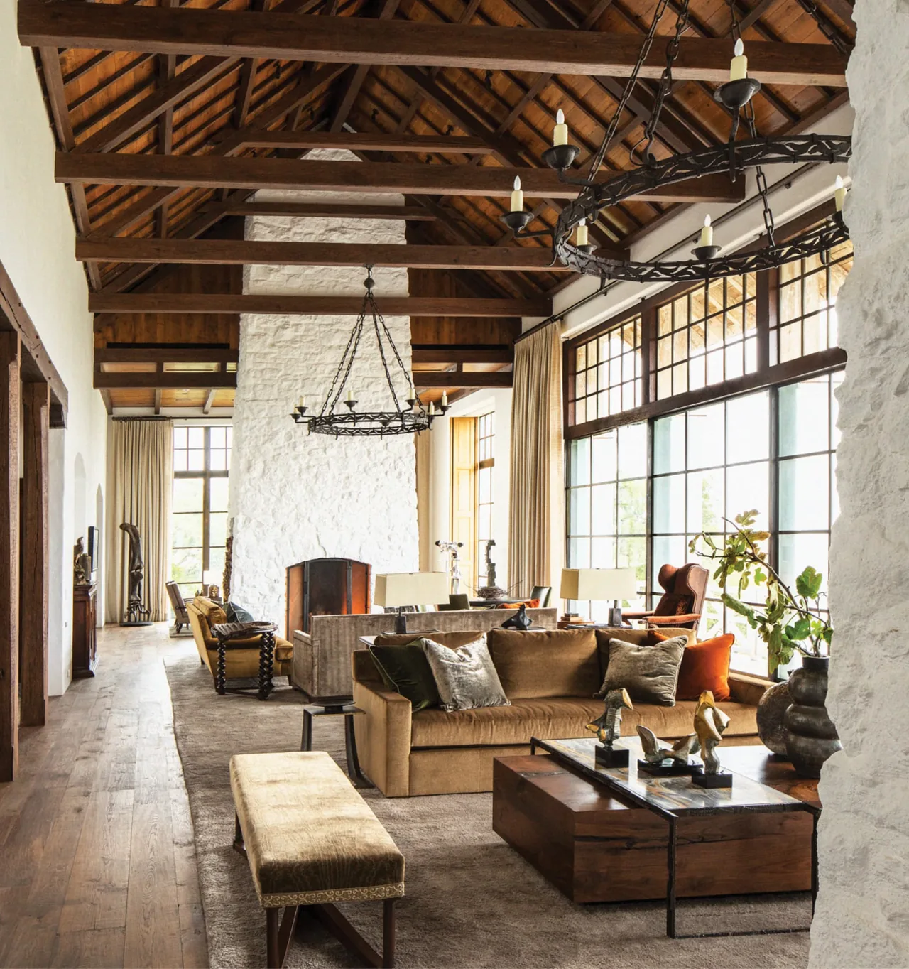 Living room features a vaulted wood beam ceiling, large steel-framed windows, and a white stone fireplace in Rancho Sabino Grande.