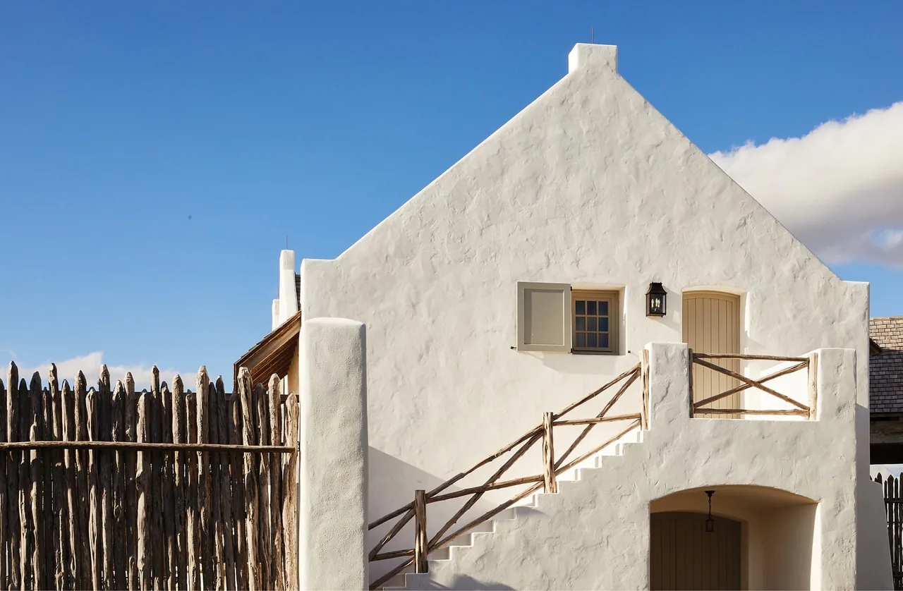 Exterior of Rancho Sabino Grande shows white textured plaster walls with wooden railings along an outdoor stairway.