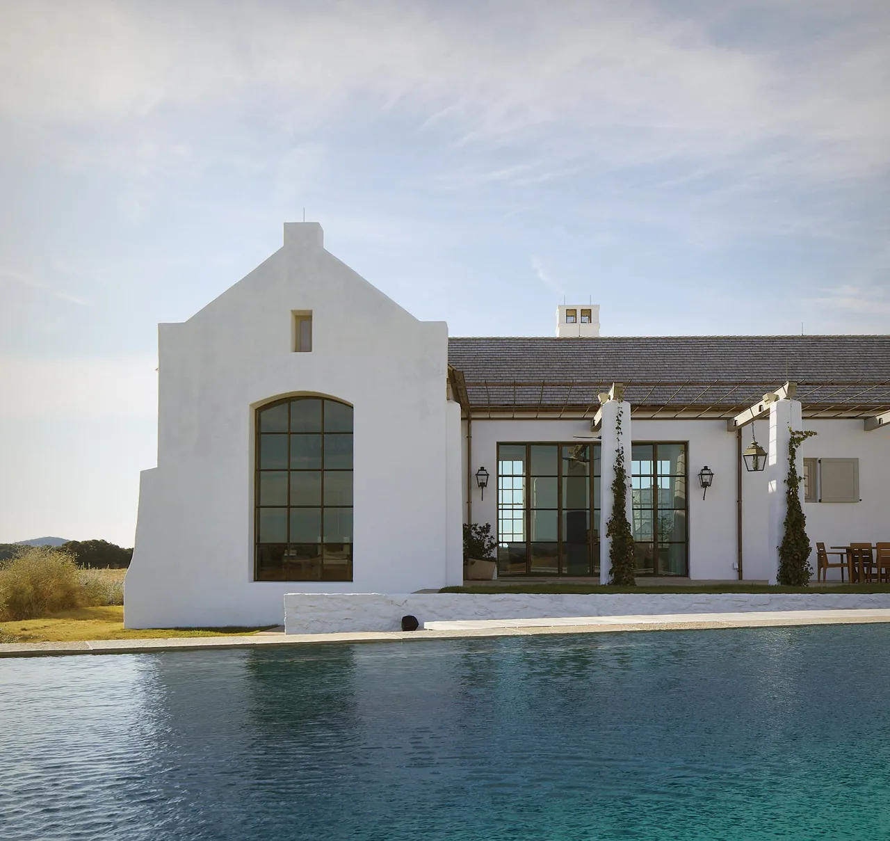 Exterior rear view of a white stucco house with large grid windows and a reflecting pool in the foreground.