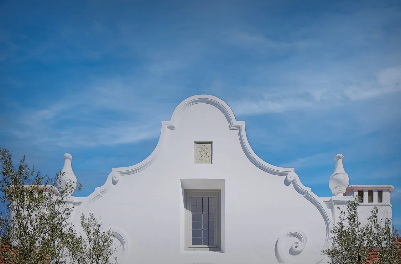 The white textured plaster exterior features a curved parapet and a small recessed window centered below an emblem plaque.