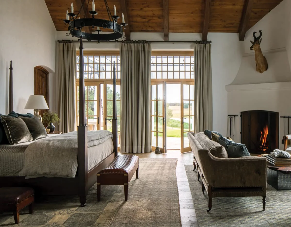 Bedroom at Rancho Sabino Grande features a wooden vaulted ceiling, a fireplace, and floor-to-ceiling glazed doors opening to a landscape view.