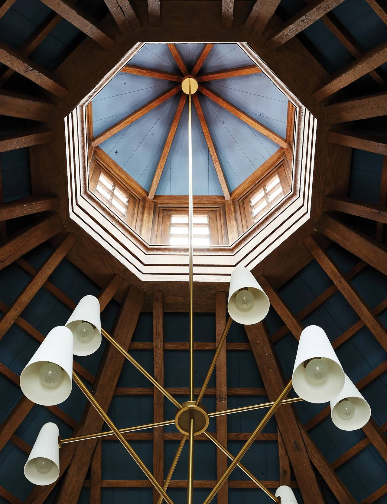 Octagonal ceiling with wood beams and a multi-arm chandelier below a skylight.