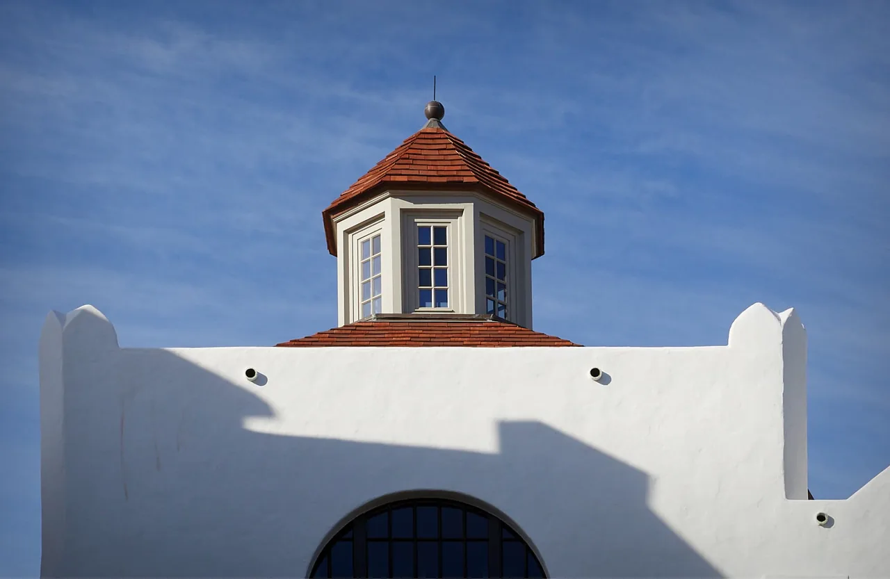Cupola with terracotta tiled roof sits atop white stucco building with arch window below.