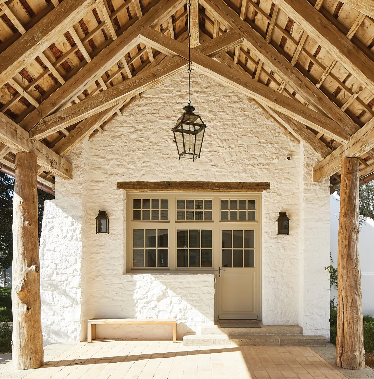 Exterior of Rancho Sabino Grande features a textured plaster stone wall with a wooden-framed window and door beneath a timber roof.