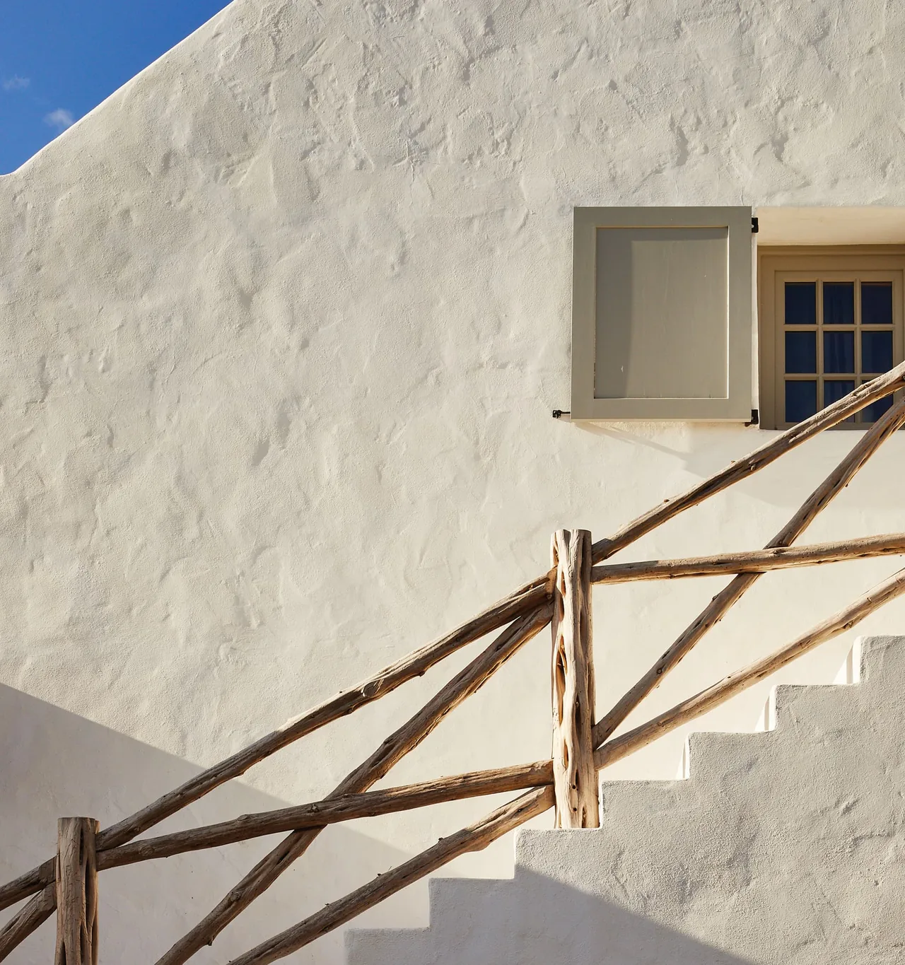 White plaster wall with a grid window and natural wooden handrail on exterior stairs at Rancho Sabino Grande.