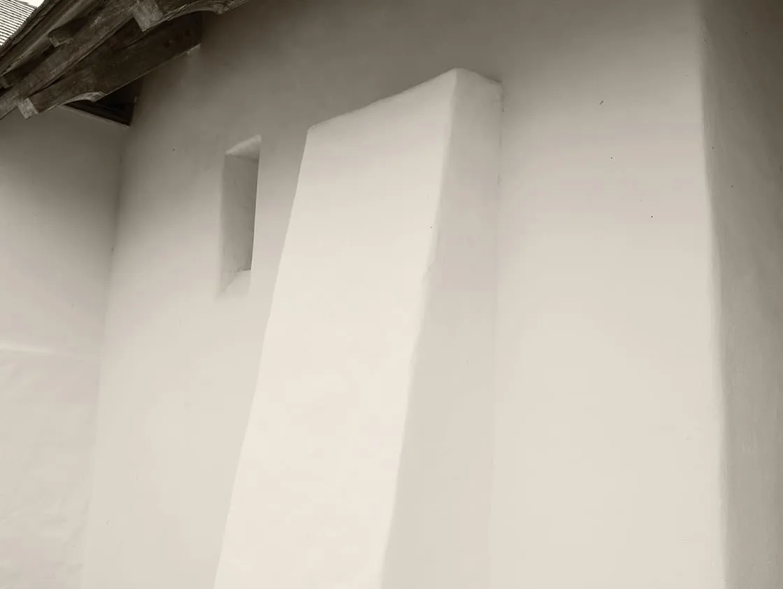 White plaster exterior wall with small recessed window and wooden eaves at Rancho Sabino Grande.