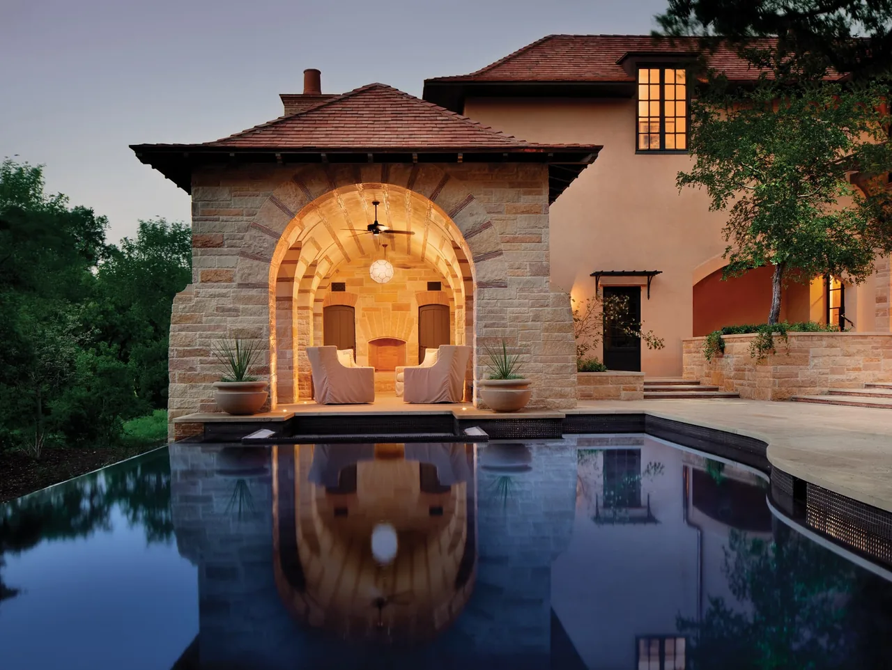 The Turnberry project features a stone pavilion with arched openings, seating, and a pool reflecting its warm lighting in the evening.