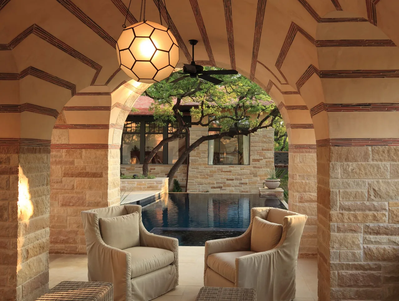 Vaulted arched stone porch with seating overlooking a modern pool and natural stone exterior.