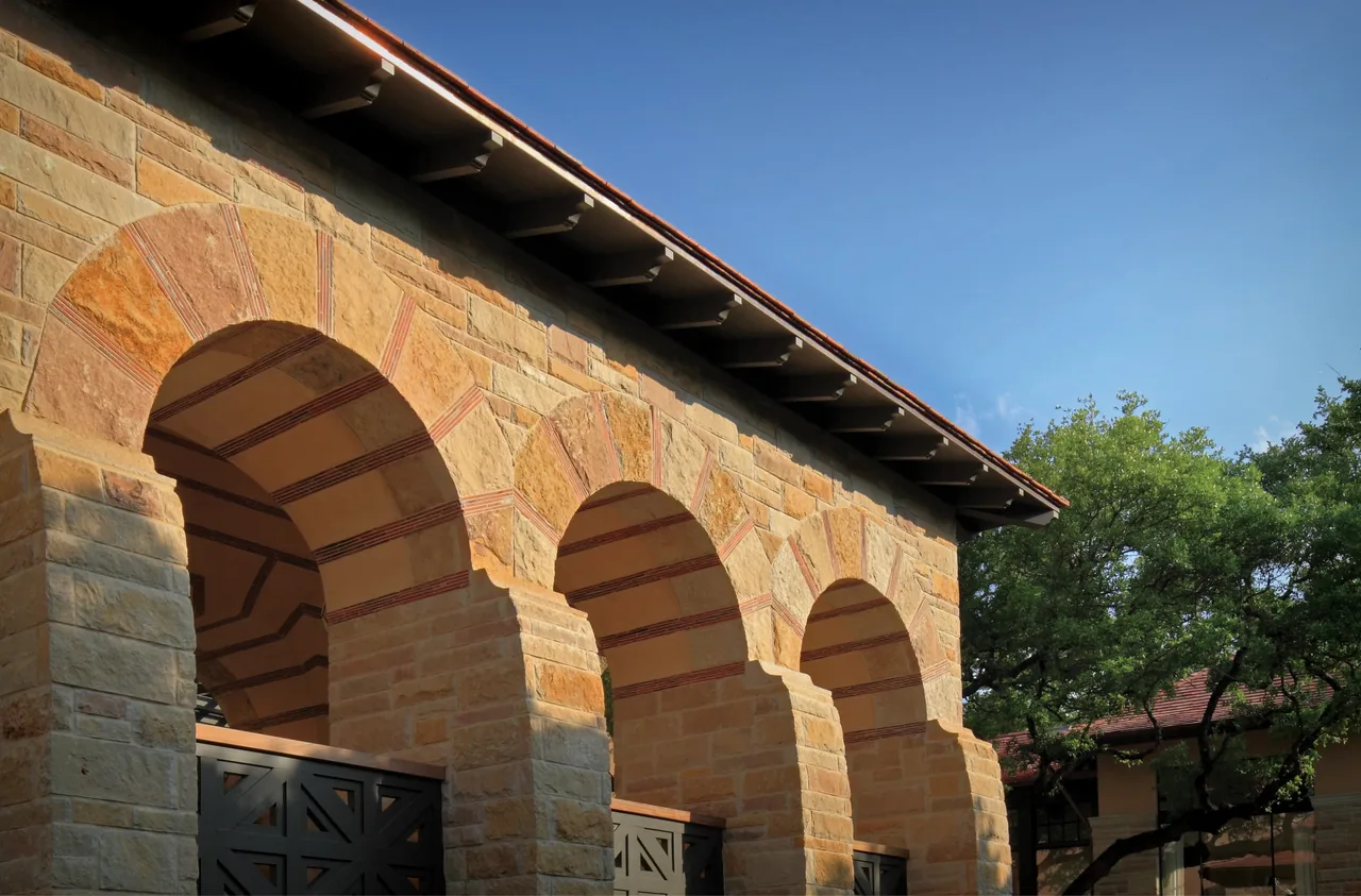 Stone arches form the front facade under a tiled roof with exposed eaves of the Turnberry project.