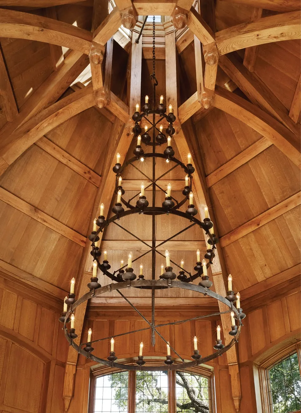 Wrought iron chandelier suspended from a timber vaulted ceiling with exposed beams and skylight.