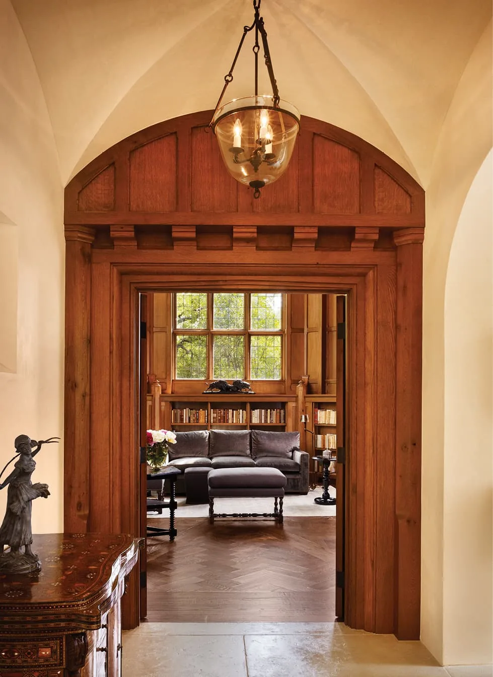 Living room view through a detailed arched wood doorway with built-in bookshelves and large window.