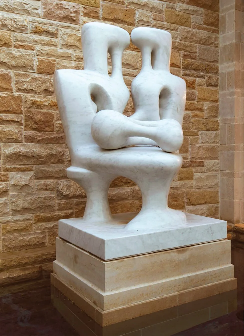 Abstract white marble sculpture of two seated figures in front of a limestone wall at the Turnberry project.