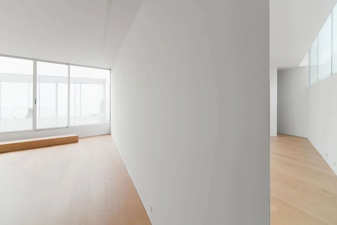 Minimalist interior with light wood flooring and a large sliding glass door opening to exterior space.