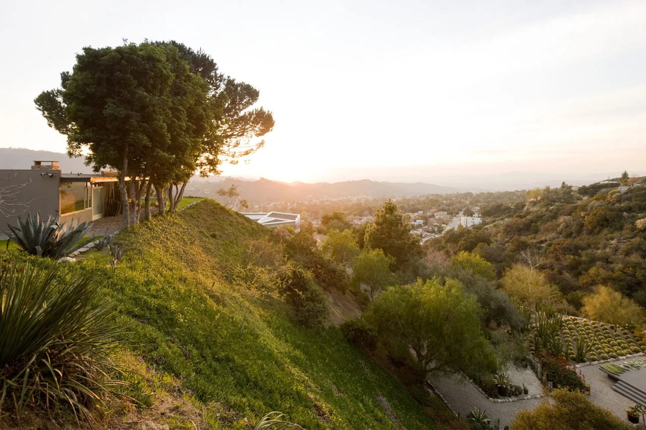 The Pittman Dowell residence sits on a hillside overlooking a lush valley with city views at sunset.