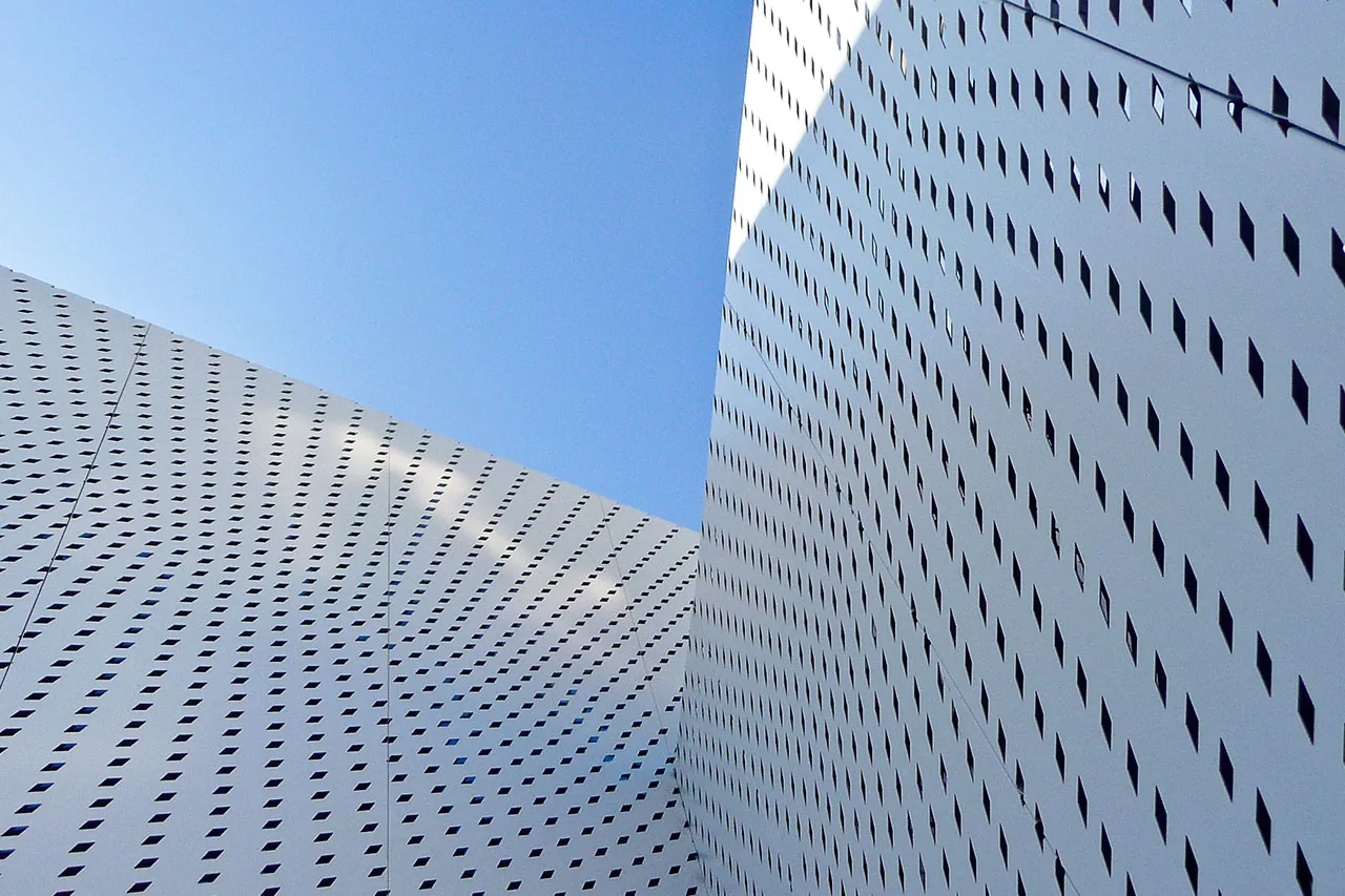 Exterior walls of a building feature a pattern of small diamond-shaped perforations under blue sky.