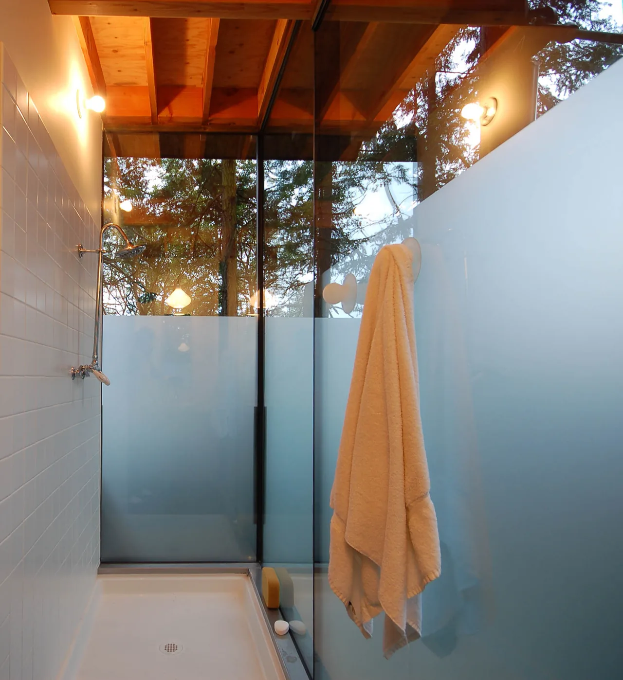 Shower area features frosted glass wall and exposed wooden ceiling beams, with a white towel hanging on a suction hook.