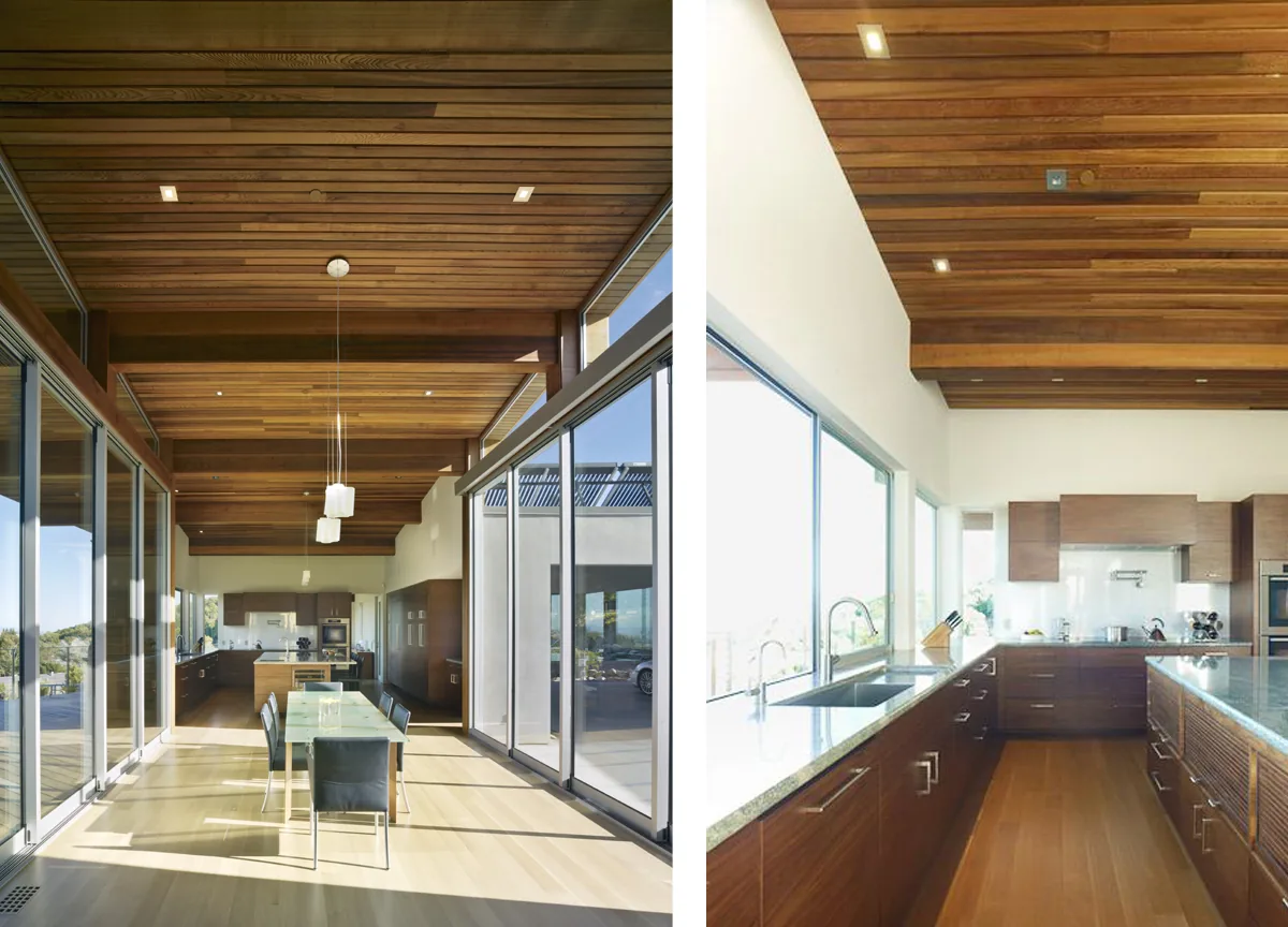 The kitchen and dining area features wood ceilings, extensive glazing with sliding glass doors, and wood cabinets with metal handles.