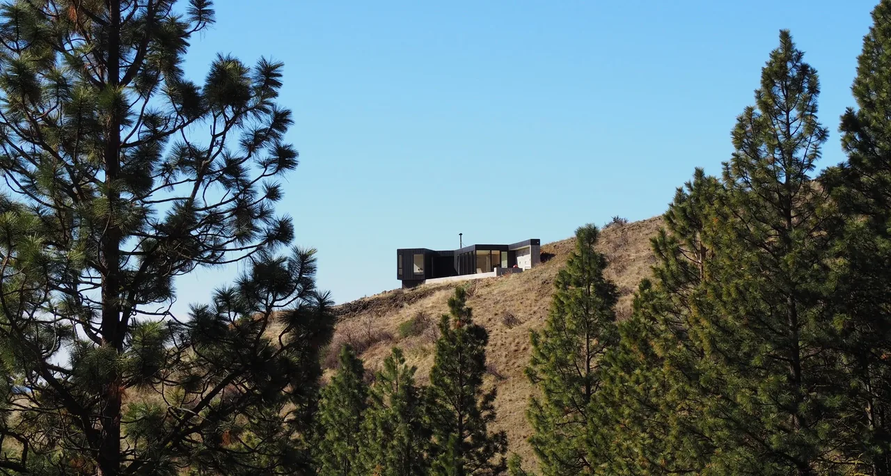 Basalt Canyon Shelter by Workshop A | D is positioned on a hilltop with views framed by surrounding pine trees.