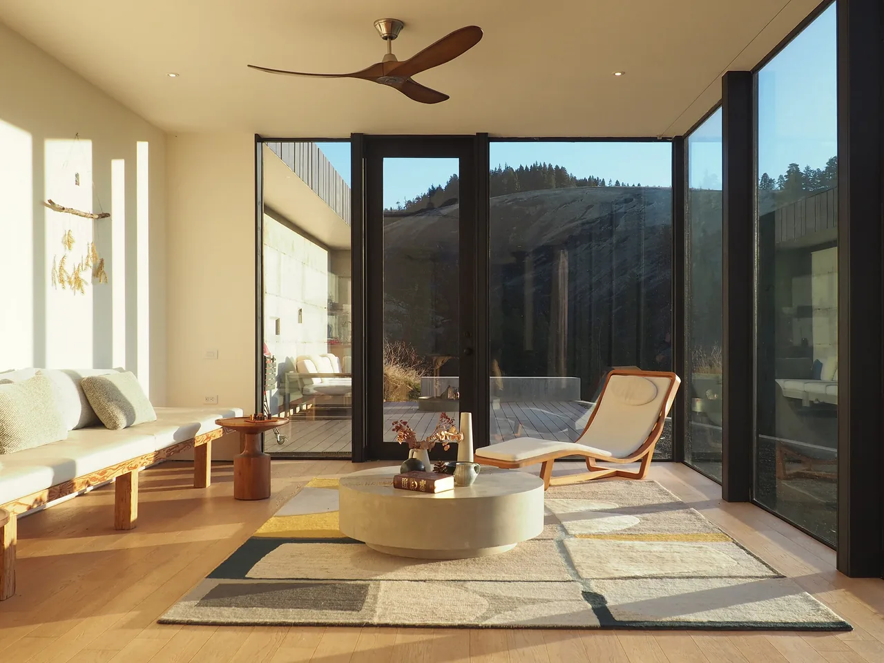 Living room in Basalt Canyon Shelter features floor-to-ceiling glazing and a modern wood lounge chair with light cushions.