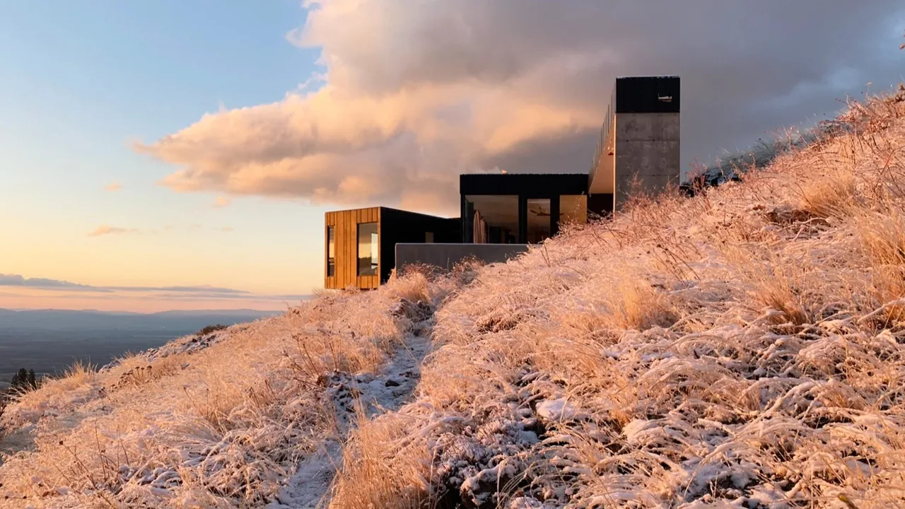 Basalt Canyon Shelter by Workshop A | D sits on a snowy hillside during sunset with expansive landscape views.
