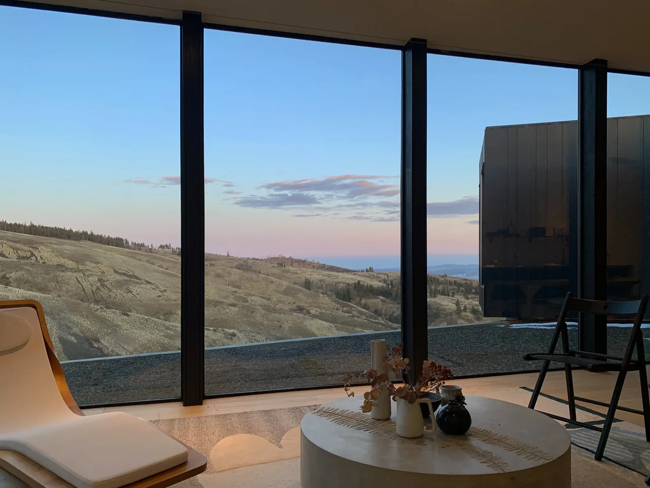 Room with floor-to-ceiling glazing frames a rolling hills view at sunset.