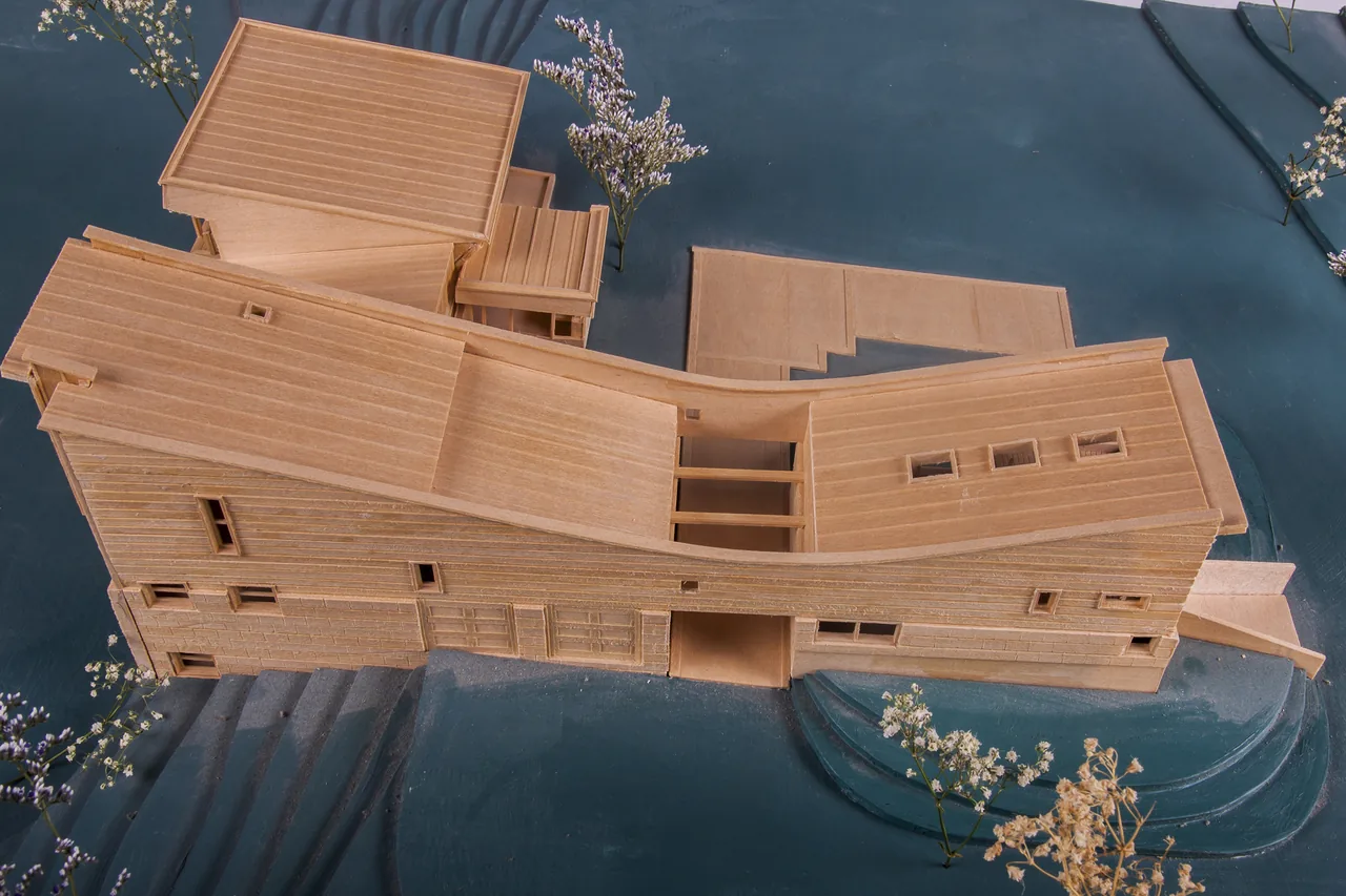 Scale model showing a multi-level house with a curved roof and multiple rectangular windows on different sides.