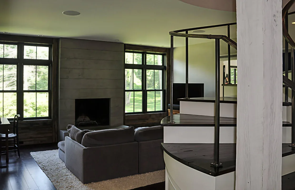 Living room features black window frames, symmetrical multi-pane windows, a central stone fireplace, and a spiral staircase.