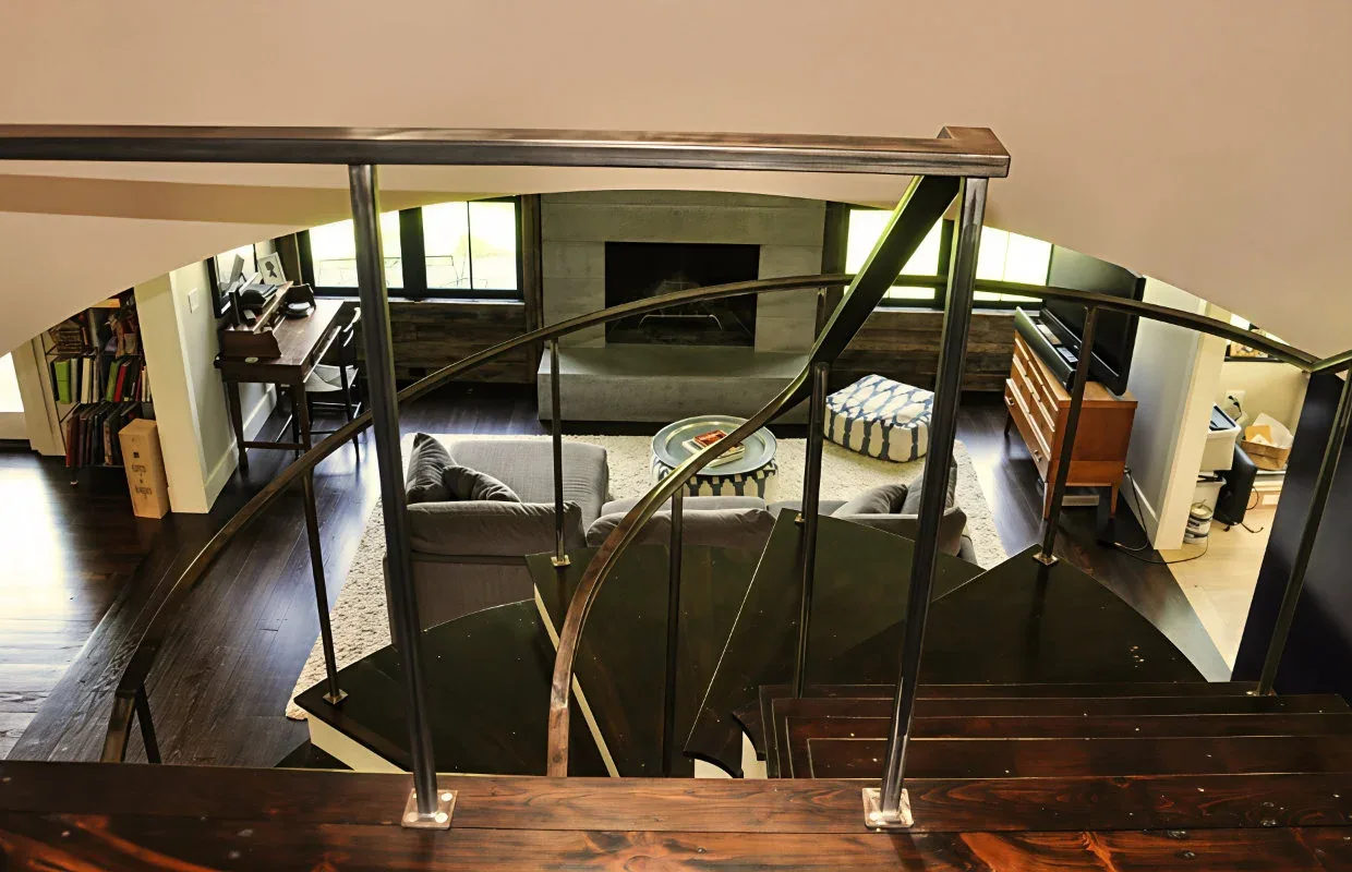 Dark wood spiral staircase with black metal railing overlooks a living room featuring a fireplace.